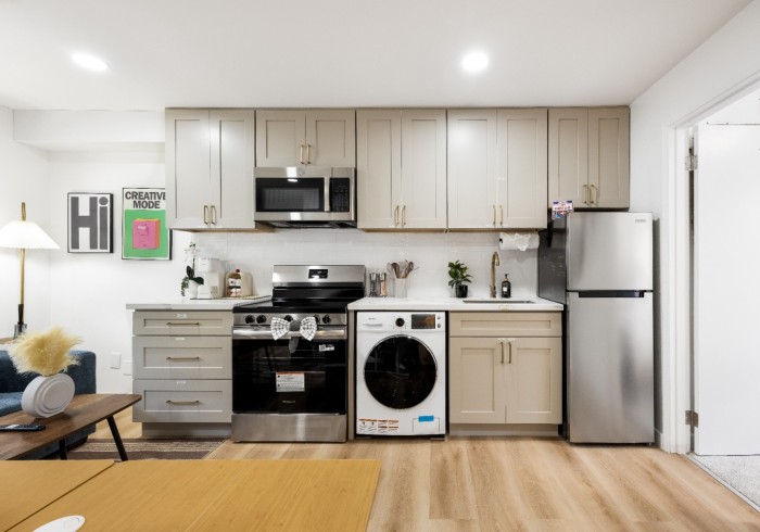 A compact kitchenette with stove, microwave, refrigerator, cabinets, and in-unit washer.