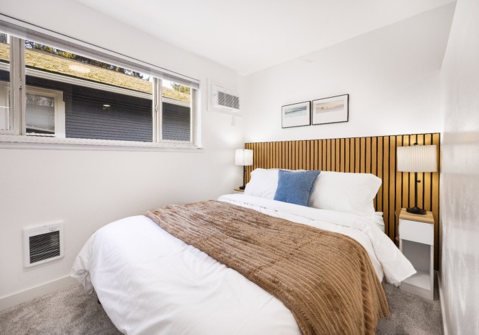 A queen bed with white linens, warm blanket, and wood slat headboard.